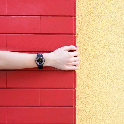 barrio chino person wearing black analog watch holding red brick wall forearm